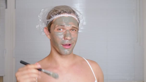 Strano uomo con la faccia piena. Un giovane fa procedure cosmetiche per il volto di una casa di fronte a uno specchio. 4k — Video Stock