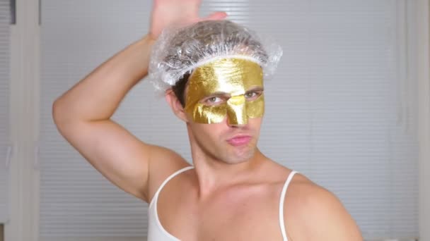 Seltsamer Mann mit Gesichtsmaske. Ein junger Mann macht kosmetische Eingriffe am Gesicht eines Hauses vor dem Spiegel. 4k, goldene Maske — Stockvideo