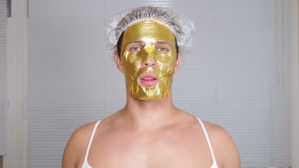 Seltsamer Mann mit Gesichtsmaske. Ein junger Mann macht kosmetische Eingriffe am Gesicht eines Hauses vor dem Spiegel. 4k, goldene Maske — Stockvideo