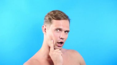 Mavi renkli arka plan üzerinde genç adam. portre. duygu ve hareketleri. 4k, yakın çekim. Ağır çekim. adam cinsel kameraya bakıyor ve onunla birlikte gitmek öneriyor.
