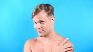 Mavi renkli arka plan üzerinde genç adam. portre. duygu ve hareketleri. 4k, yakın çekim. Ağır çekim. adam cinsel kameraya bakıyor ve onunla birlikte gitmek öneriyor.