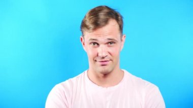 Mavi renkli arka plan üzerinde genç adam. portre. duygu ve hareketleri. 4k, yakın çekim. Ağır çekim. adam cinsel kameraya bakıyor ve onunla birlikte gitmek öneriyor.