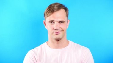 Mavi renkli bir arka plan üzerinde genç adam. portre. duygu ve hareketleri. 4k, yakın çekim. Ağır çekim. Kamera ve sevimli gülümseme adam bakar