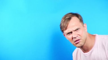 Mavi renkli bir arka plan üzerinde genç adam. portre. duygu ve hareketleri. 4k, yakın çekim. Ağır çekim. faiz ile kamera adam görünüyor. Ne olay .