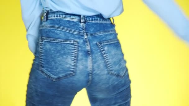 Ein Mädchen in Jeans mit schönem rundem Gesäß ist sexuell bewegend. Nahaufnahme. 4k, Zeitlupe, gelber Hintergrund — Stockvideo