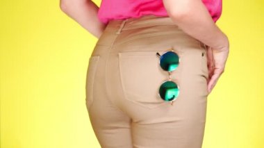 Kız şık dar bej kot pantolon ve moda aksesuarları, yuvarlak ayna güneş gözlüğü. Yaz taze tarzı. yakın çekim, 4k, yavaş hareket, sarı arka plan renkli