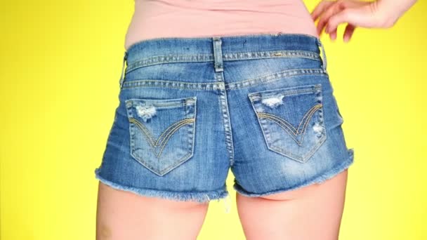 Meisje in korte broek de korte jeans blauw. Close-up beeld van achteren. Zomer frisse stijl. 4k, slow-motion. gekleurde gele achtergrond — Stockvideo