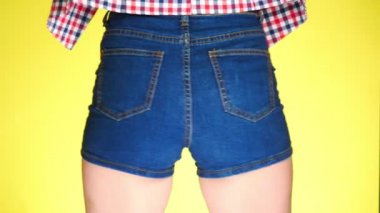 Kısa kot mavi şortlu kız. Arkadan yakından görmek. Yaz taze tarzı. 4k, ağır çekim. renkli sarı arka plan