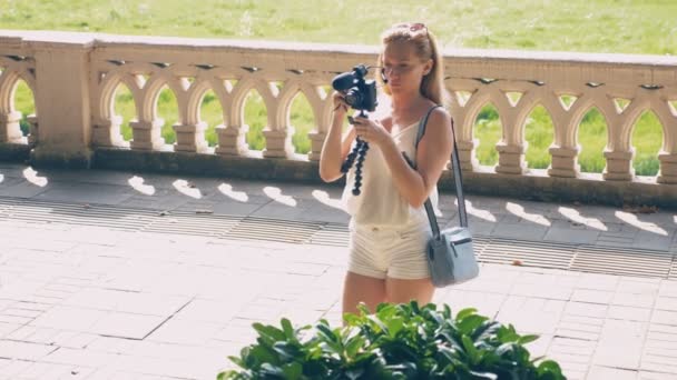 Bela blogueira mulher feliz com uma câmera, leva sua reportagem passeando ao longo do aterro da cidade resort. 4k, câmera lenta . — Vídeo de Stock
