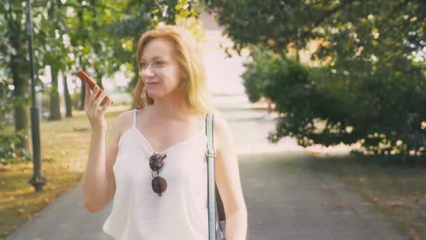 Gelukkig jonge vrouw praten over de telefoon, wandelen langs de waterkant op een warme zonnige zomerdag. 4k, slow-motion — Stockvideo