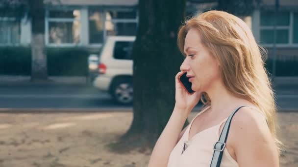 Mujer joven y feliz hablando por teléfono, caminando por el paseo marítimo en un caluroso día soleado de verano. 4k, cámara lenta — Vídeos de Stock