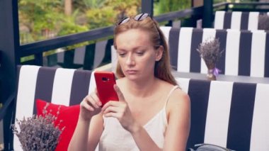 Ayrılık ile mutsuz olmak telefon bakarak kafede masada oturan bir genç bayan. 4k, ağır çekim, şık kafe iç. Siyah ve beyaz çizgili ve kırmızı vurgu