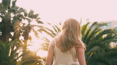 Bir palmiye ağacı yol boyunca yürüyüş güzel şık sarışın kadın güneş gözlüğü. Palmiye gözlükte yansıtılır. 4 k yavaş hareket.