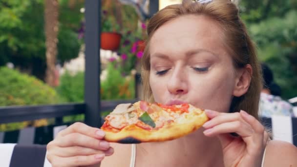 Hermosa joven comiendo una rebanada de pizza en la cafetería. primer plano, 4k, cámara lenta — Vídeo de stock