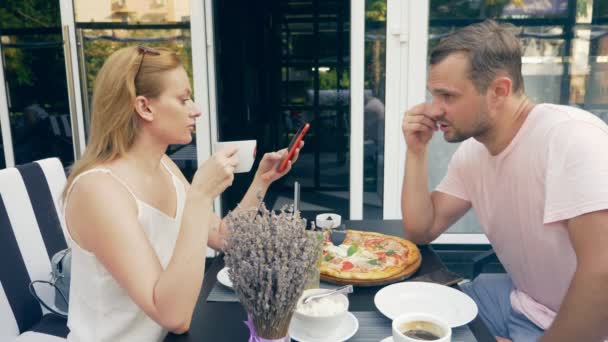 Pareja en un café al aire libre. Hombre y mujer en una cita. un socio mira su teléfono, el segundo trata de hablar con él. 4k, cámara lenta . — Vídeos de Stock