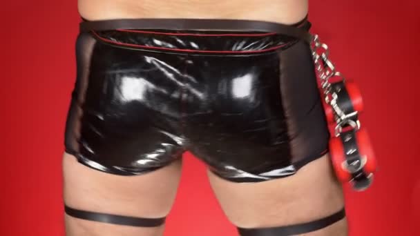 Sexy muž model v prádle na červeném pozadí. muž v černé latexové kalhoty přesune jeho boky. 4k, zpomalené. detail — Stock video