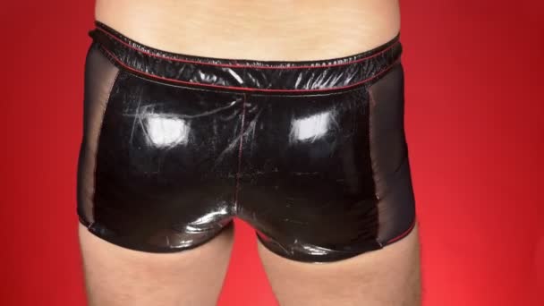 Σέξι ανδρικό πρότυπο στο εσώρουχο σε κόκκινο φόντο. ένας άνθρωπος σε μαύρο λατέξ παντελόνι μετακινεί τα ισχία. 4k, αργή κίνηση. γκρο πλαν — Αρχείο Βίντεο