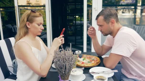 Couple in an outdoor cafe. Man and woman on a date. one partner looks at his phone, the second tries to talk to him. 4k, slow motion. — Stock Video