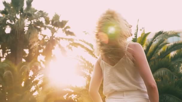 Vacker elegant blond kvinna i solglasögon, promenader längs en palm tree sökväg. Handflatan återspeglas i glas. 4 k slowmotion. — Stockvideo