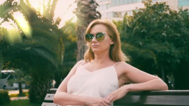 Bir palmiye ağacı yol boyunca yürüyüş güzel şık sarışın kadın güneş gözlüğü. Palmiye gözlükte yansıtılır. 4 k yavaş hareket.