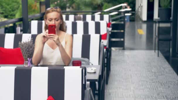 Jonge vrouw zittend aan tafel in café kijken naar telefoon wordt ongelukkig met uiteenvallen. 4k, Slowmotion, stijlvolle café interieur. Strepen zwart-wit en rood accent — Stockvideo