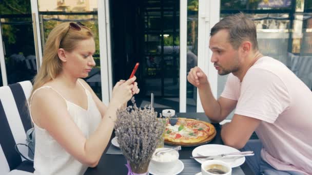 在室外咖啡馆的情侣。男人和女人约会。一个合伙人看着他的手机, 第二次试图和他说话。4k. 慢动作. — 图库视频影像