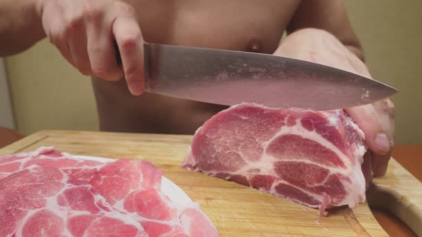 裸の胴体を持つ男は、スローモーションでナイフで生の肉をカットします。4 k、クローズ アップ — ストック動画