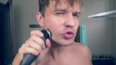 komik bir yakışıklı adam banyoda bir elektrikli tıraş makinesi ile sakalını tıraş ve bir ayna önünde şarkı söylüyor. 4k.