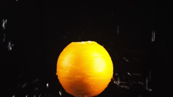 Orange, gros plan. Des gouttes d'eau tombent sur une pomme tournante sur un fond noir. super ralenti . — Video