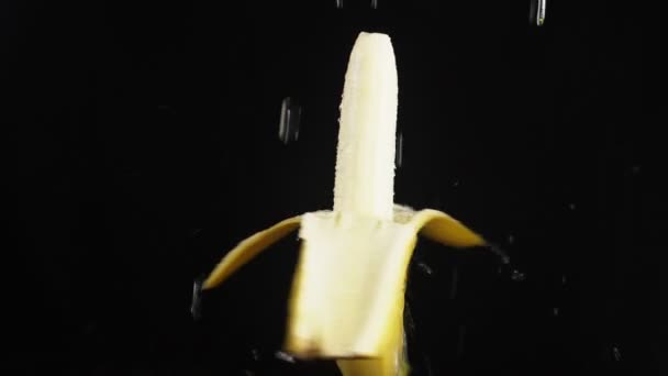 Gepelde banaan, sluiten - omhoog. Druppels water vallen op een roterende apple op een zwarte achtergrond. Super slow-motion. — Stockvideo