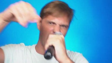 deli, komik ve genç bir adam, bir mikrofona şarkı söylüyor. renkli arka planı, yakın çekim. 4k, ağır çekim