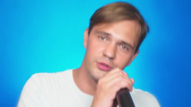 deli, komik ve genç bir adam, bir mikrofona şarkı söylüyor. renkli arka planı, yakın çekim. 4k, ağır çekim