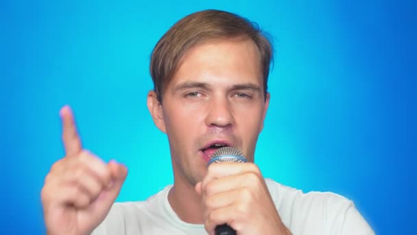 Egy őrült vicces fiatalember dalokat énekel a mikrofonba. színes háttér, zár-megjelöl. 4k, lassú mozgás — Stock videók