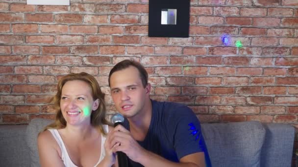 Paar singt Lied - Karaoke-Team. Mann und Frau singen Lieder in ein Mikrofon, das auf der Couch sitzt. 4k, Zeitlupe — Stockvideo