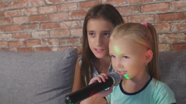 两个小女孩正在用麦克风唱歌。歌曲在家庭卡拉 ok。4k、慢动作、特写 — 图库视频影像