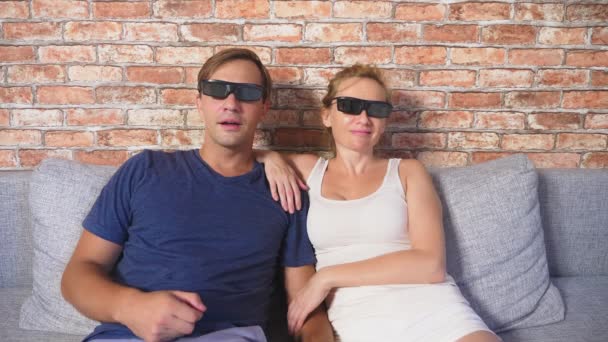 Nahaufnahme. Ein junges Paar in Brille sitzt auf dem Sofa im Wohnzimmer und schaut sich den Film an. 4k, Zeitlupe. — Stockvideo