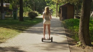Beyaz şortlu kız açık güneşli bir günde bir Segway sürme. parlama yaz park ve güneş. 4k, ağır çekim silah, stadikam atış