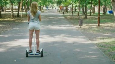 Beyaz şortlu kız açık güneşli bir günde bir Segway sürme. parlama yaz park ve güneş. 4k, ağır çekim silah, stadikam atış