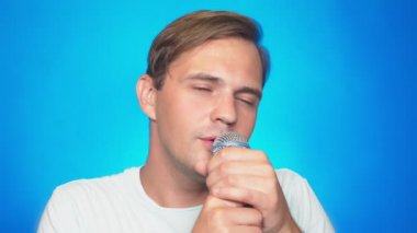 deli, komik ve genç bir adam, bir mikrofona şarkı söylüyor. renkli arka planı, yakın çekim. 4k, ağır çekim