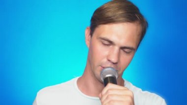 deli, komik ve genç bir adam, bir mikrofona şarkı söylüyor. renkli arka planı, yakın çekim. 4k, ağır çekim