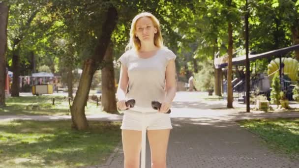 Fille en short blanc, chevauchant un Segway par une journée ensoleillée claire. parc d'été et soleil éblouissant. 4k, tir au ralenti, tir au stadikam — Video