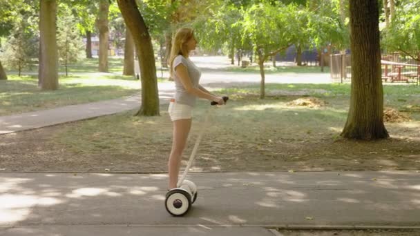 晴れた日に、セグウェイに乗って白いパンツの女の子。公園の夏し、太陽のまぶしさ。4 k、スローモーション撮影、stadikam ショット — ストック動画