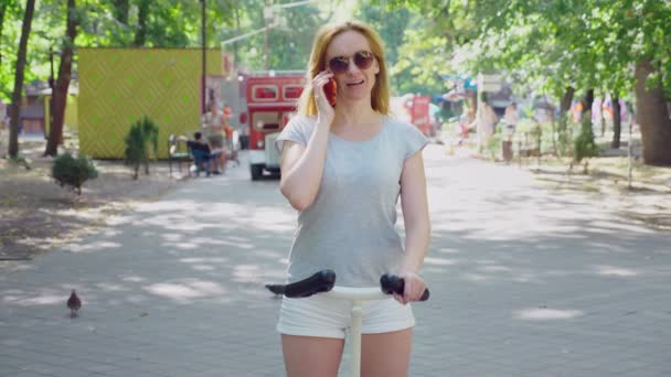 Girl in white shorts, riding a Segway on a clear sunny day. summer park and sun glare. 4k, slow-motion shooting, stadikam shot — Stock Video