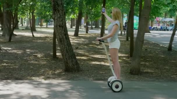 Beyaz şortlu kız açık güneşli bir günde bir Segway sürme. parlama yaz park ve güneş. 4k, ağır çekim silah, stadikam atış — Stok video
