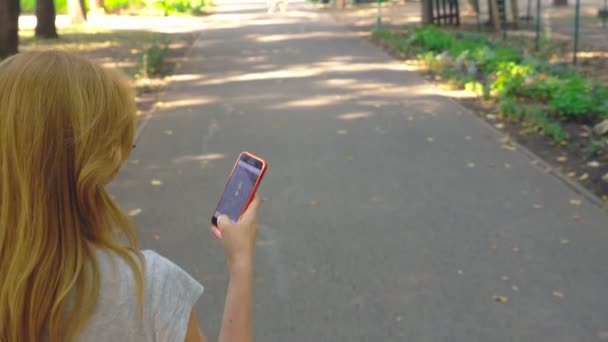 Kvinna kommer till parken med sin telefon på sommardag under solen ljus. 4 k, slow motion, standicam skott — Stockvideo