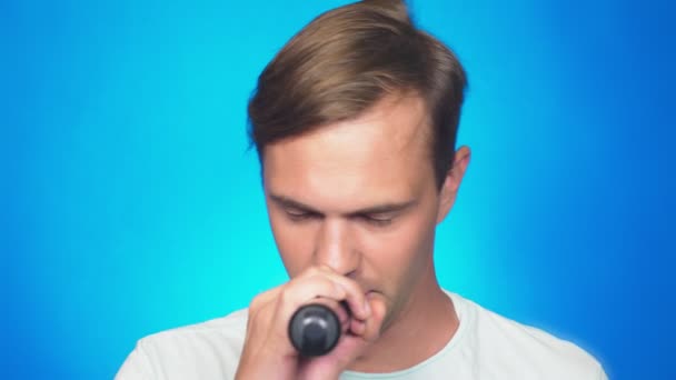 Egy őrült vicces fiatalember dalokat énekel a mikrofonba. színes háttér, zár-megjelöl. 4k, lassú mozgás — Stock videók
