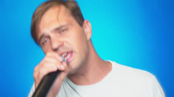 Bláznivý srandovní mladý muž zpívá písně do mikrofonu. Barva pozadí, detail. 4k, pomalý pohyb — Stock video