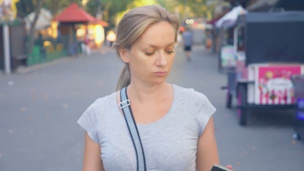 Mulher vai estacionar com seu telefone no dia de verão sob a luz do sol. 4K, câmera lenta, tiro em pé — Vídeo de Stock