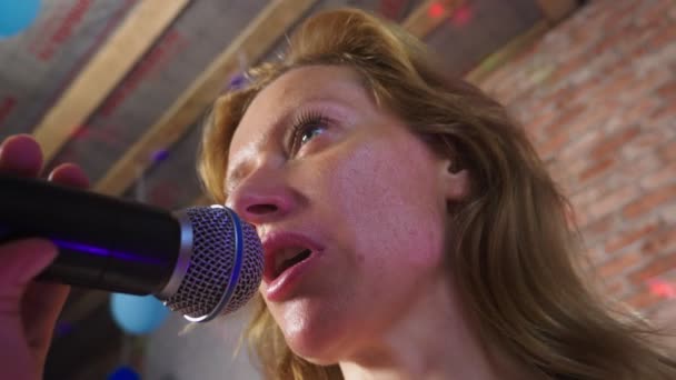 De cerca. una mujer gritando a un micrófono. una mujer canta karaoke en un micrófono en un entorno familiar. 4k, cámara lenta — Vídeo de stock