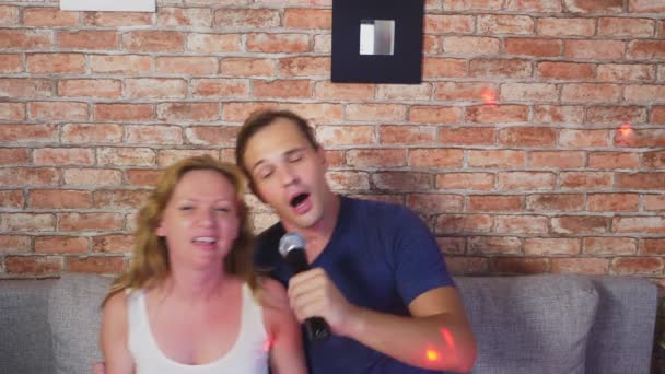 Pár énekelt dal - csapat karaoke. pár férfi és a nő énekelnek a mikrofonba, ül a kanapén. 4k, lassú mozgás — Stock videók